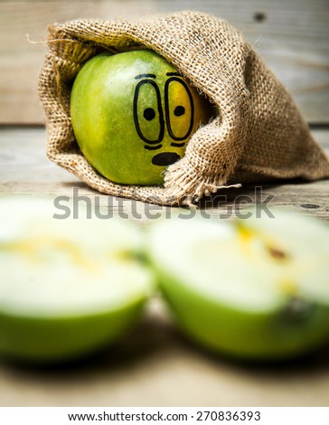 Knife slice apple on wooden background. Apple with painted face in shock
