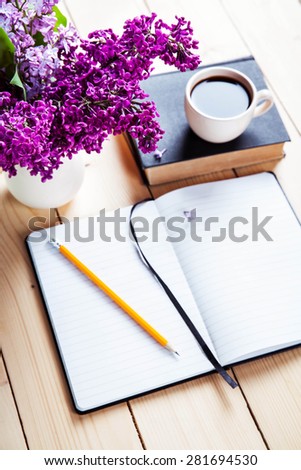 Beautiful lilac on office desk with a book and a cup of coffee and notebook