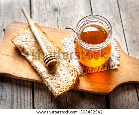 Honey in a jar, slice of bread, wheat and milk on an old vintage planked wood table from above. Rural or rustic style breakfast concept. Background layout with free text space.