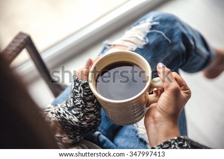 Girl\'s hands holding a cup of coffee, ripped jeans. Fashion manicur