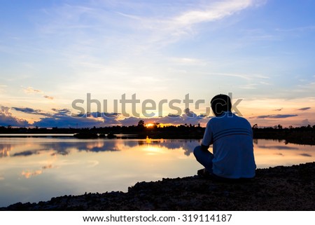man sit down and take photo by camera at lake with sunset sky.