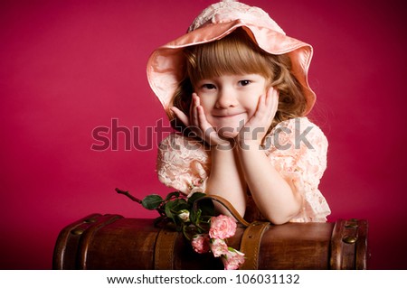 Portrait of little smiling girl with rose flower laying on wooden trunk, against red background