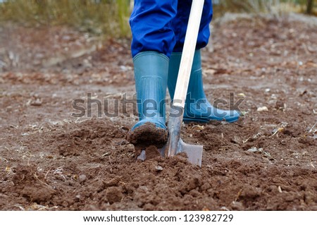 Close up of a man digging soil with shovel in rubber boots and gloves