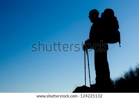 Silhouette of hiking man with backpack and hiking poles, blue sky background