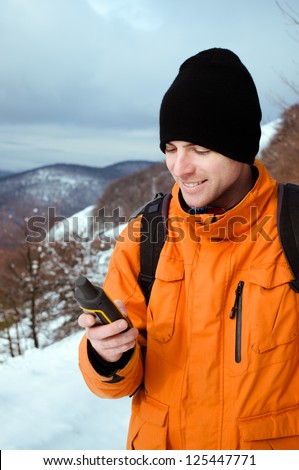 Portrait of backpacker looking at GPS navigator, Global Positioning System device. Mountain winter landscape as a background.