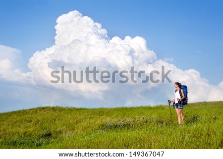 Smiling hiking young woman with backpack and trekking poles walking in a green meadow