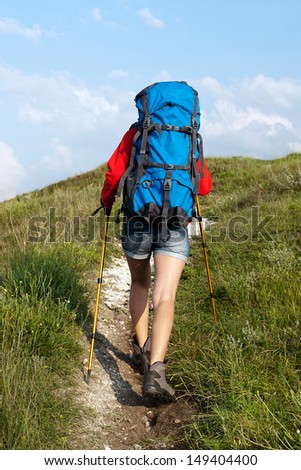 Hiking young woman with backpack and trekking poles on the mountain trail