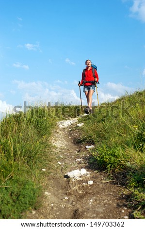 Smiling hiking young woman with backpack and trekking poles on the mountain trail
