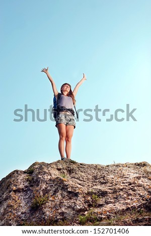 Happy young woman standing on the top of mountain with raised hands