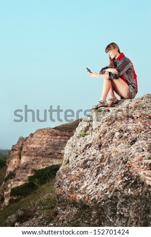Portrait of a smiling young woman sitting on the top of mountain and looking at GPS (Global Position System)