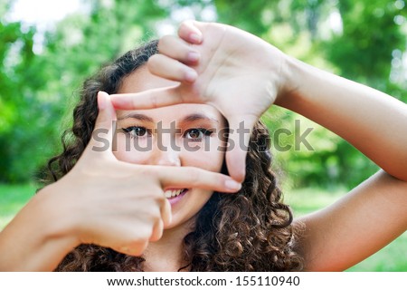 Portrait of a smiling teenage girl showing frame by hands