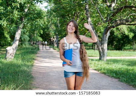 Portrait of a beautiful teenage girl with long braid in the park saying hello to somebody