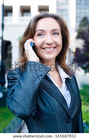 Portrait of young smiling business woman talking cell phone, walking on the street