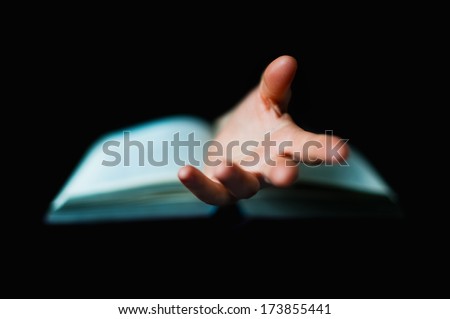 Hand protruding out from an open book, isolated on black background, reading concept