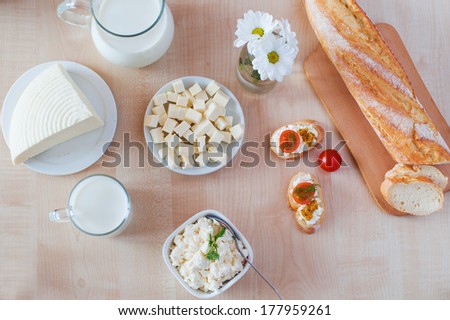 Breakfast with cottage cheese, glass of milk, bulgarian cheese and sandwiches, on white wooden table