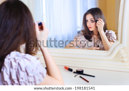 Portrait of  beautiful young woman looking at the mirror putting mascara holding a makeup brush
