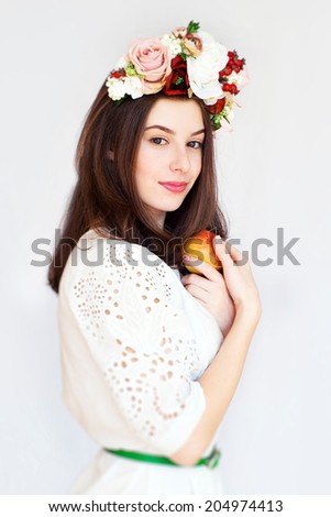 Portrait of beautiful girl with flower wreath eating apple, light background