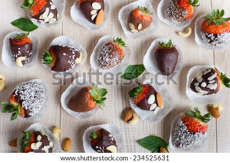 Variety of strawberries covered with a milk, dark and white chocolate and nuts, on the light wooden table