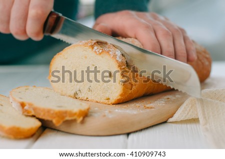 Male hands cutting wheaten bread on the wooden board, selective focus