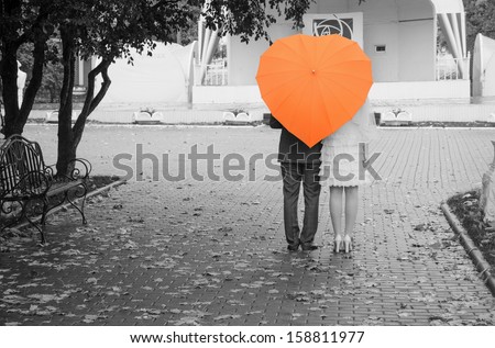 Lovers couple on a black and white photo of an orange umbrella. Rear view.