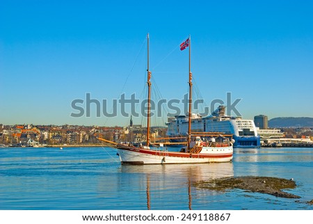OSLO, NORWAY - APRIL 12, 2010: Bygdoy Peninsula. Sailing ship with norwegian flag against the background of the coast of Oslo and cruise liner