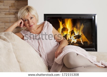 Beautiful adult blond sitting beside the fireplace at home