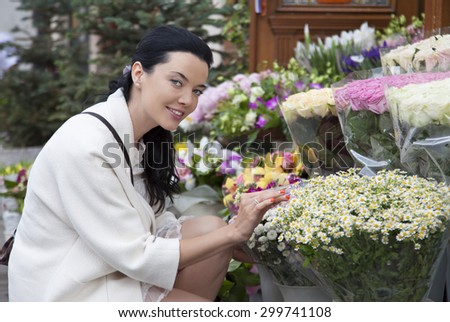 Attractive young woman shopping in an outdoors fresh flowers market stall, buying and picking from a large variety of colorful floral bouquets