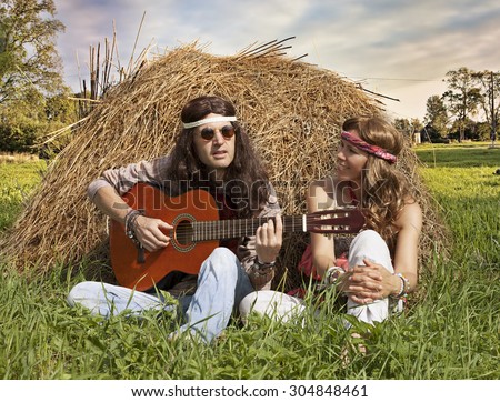 Hippie couple  playing guitar on the haystack in the midst of rural meadow
