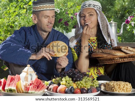 Couple dressed in Uzbekistan clothes have breakfast with fruits and flat cake