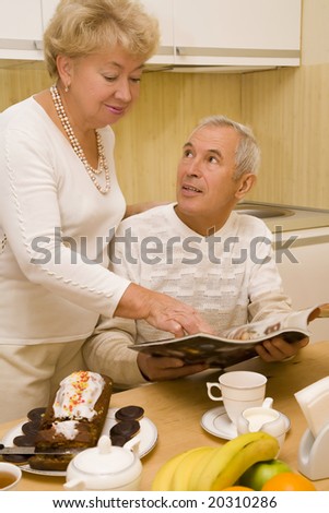 Elderly couple look a magazine during breakfast