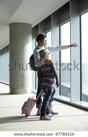Mother with daughter look through window of airport lobby