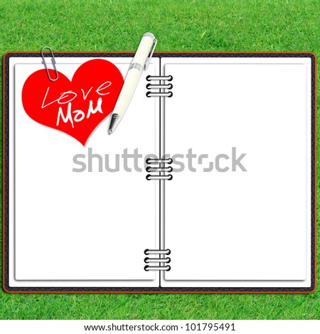 Paper note book leather cover with pen and red heart paper over grass