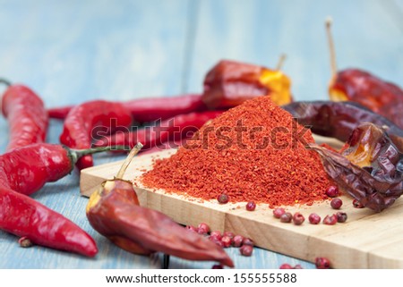 Red chilli pepper piece, and ground pepper on a wooden board.