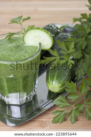 Smoothie of cucumber, parsley and celery in a glass and vegetables on a tray on the table.