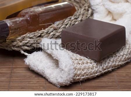 Chocolate soap on a white sponge, body oil, shampoo, gel   for body  in a basket and towel nearby.