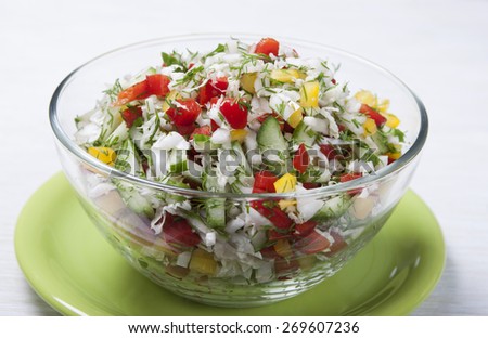 Vegetable salad with Chinese cabbage, cucumbers, bell red and yellow peppers, dill in a glass salad bowl on a green plate.
