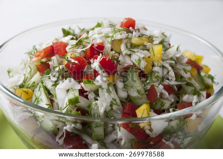 Vegetable salad with Chinese cabbage, cucumbers, bell red and yellow peppers, dill in a glass salad bowl close-up.