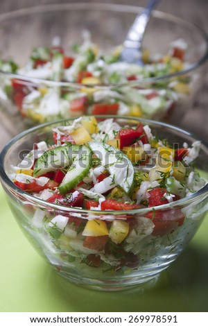 Vegetable salad with Chinese cabbage, cucumbers, bell red and yellow peppers, dill in a glass salad bowl on a green plate. In the background, a large salad bowl.
