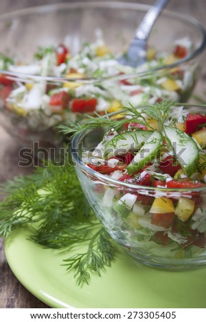 Vegetable salad with Chinese cabbage, cucumbers, bell red and yellow peppers, dill in a glass salad bowl on a green plate. In the background, a large salad bowl.