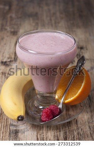 Smoothie of banana, orange juice , frozen raspberry   with yogurt in a glass on a wooden table.