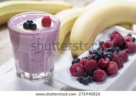Smoothies of frozen raspberries, blueberries and banana with yogurt. Blueberries and raspberries on a white plate and a banana  on a wooden table.