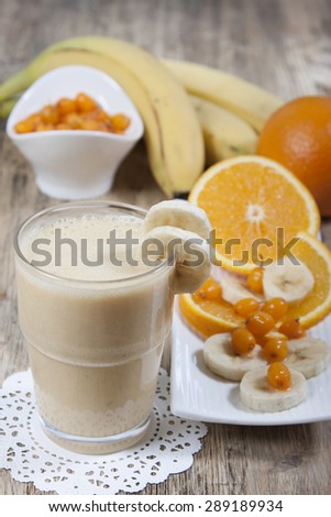 Smoothie of banana, orange juice, frozen sea-buckthorn berries with yogurt in a glass. Bananas, oranges and sea buckthorn in the background on a wooden  table.