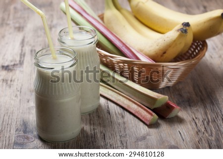 Smoothie of banana and rhubarb with yogurt in a glass. Bananas and rhubarb in a basket in the background on a wooden table.