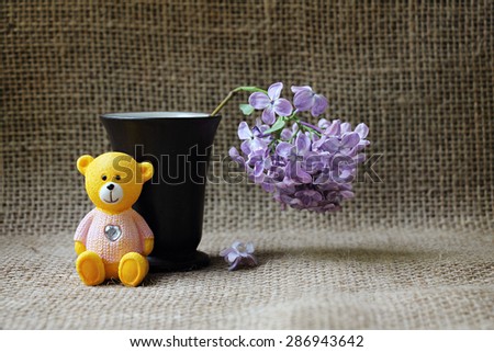 Still Life with a teddy bear and a sprig of lilac on a background of burlap. Background for greeting card for any holiday.