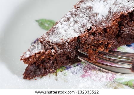 A piece of Chocolate cake powdered with Sugar on a plate with a fork.