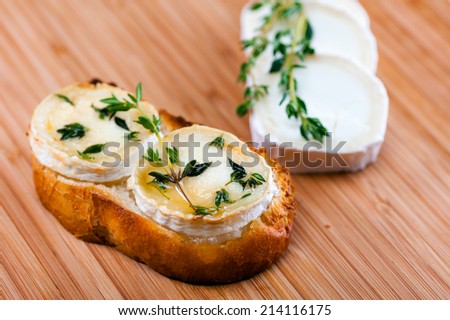 Goat cheese on a slice of bread, au gratin with honey and seasoned with Thyme. Displayed on a cutting board of Bamboo.