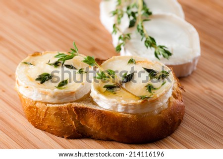 Goat cheese on a slice of bread, gratinated with honey and seasoned with Thyme. Displayed on a cutting board of Bamboo.