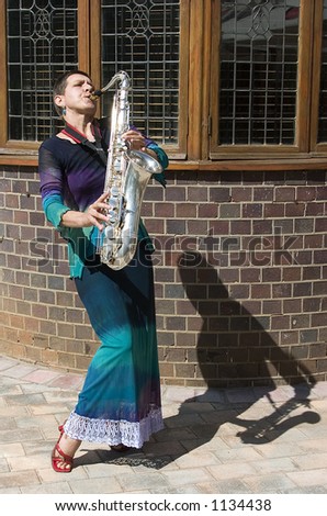 Woman playing saxophone outside with shadow to her left in front of old building.