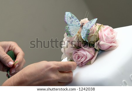 Decorating white wedding cake with roses and butterfly.
