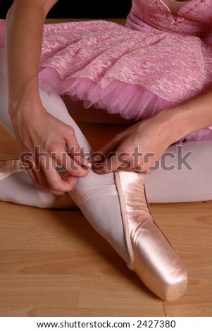 Closeup of ballerina with pink tutu siting on ground fastening shoes